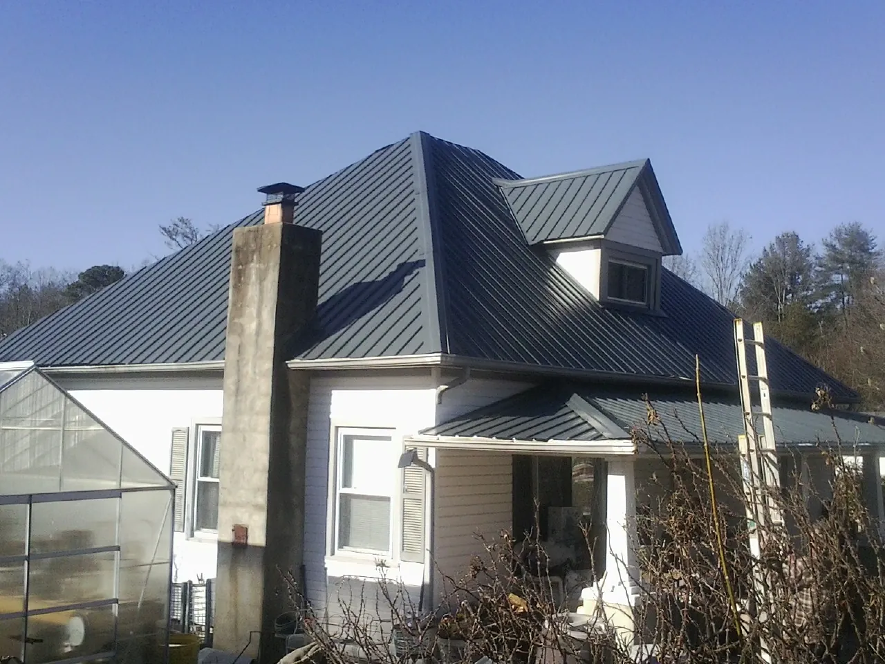 Dark blue standing seam metal roof on a white farmhouse with dormer — Slate & Tile Roof Repair by Roofing Brothers in Graytown