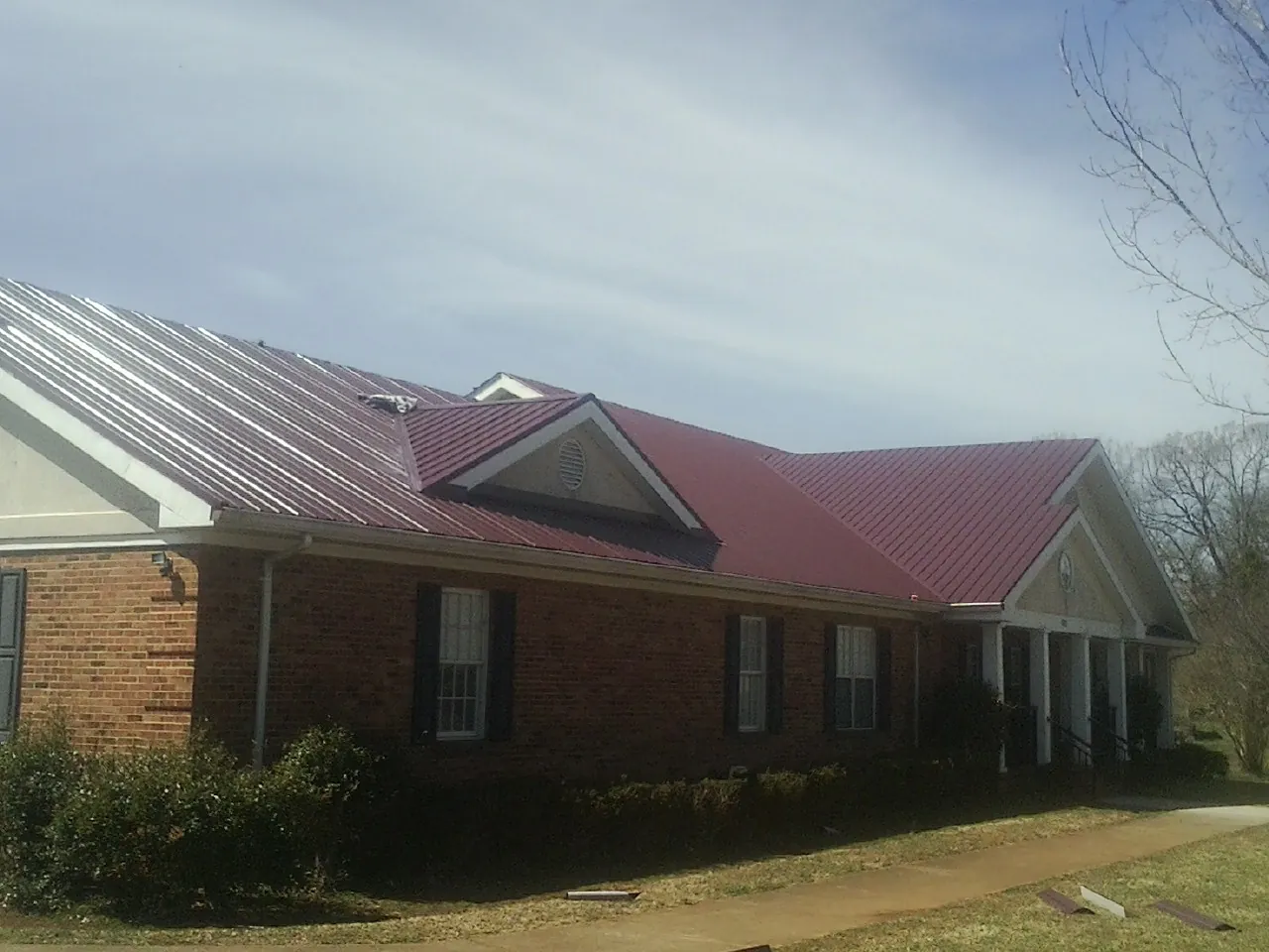 Red metal roof with gabled entries on a long brick building, from a Hail Damage Roof Repair job in Graytown