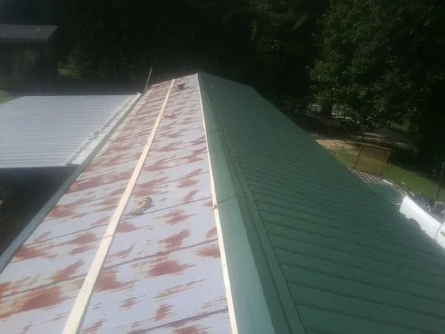Old rusted panels beside newly installed green metal roofing — Wind Damage Roof Repair by Roofing Brothers in Graytown