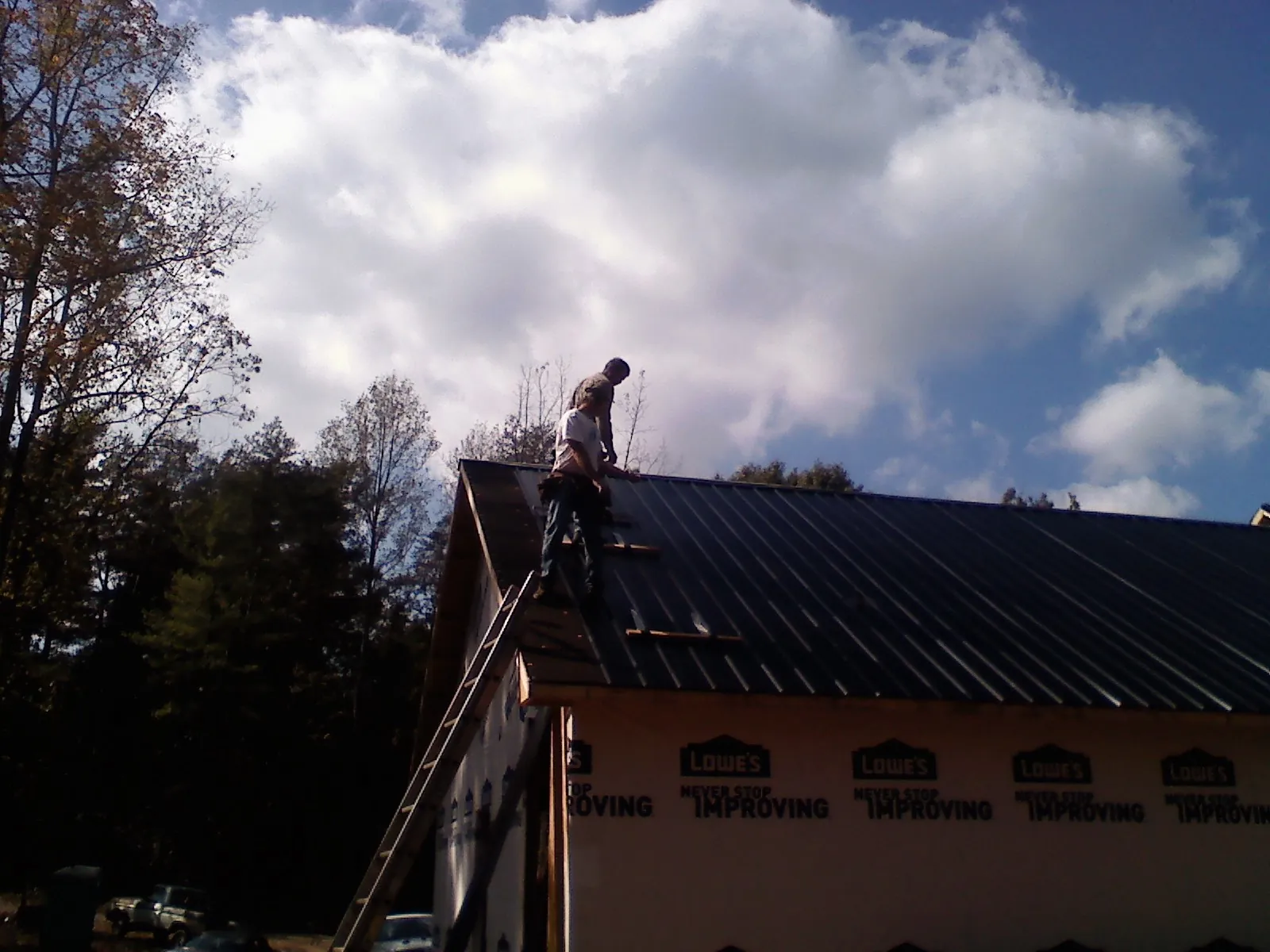 Roofer fastening dark metal panels high against a cloudy sky, from a Roof Inspection job in Graytown