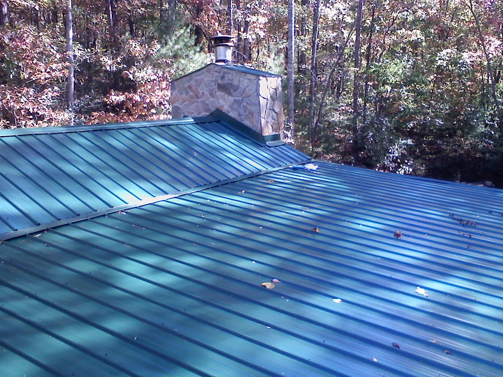 New green metal roof and stone chimney surrounded by autumn woods in Graytown